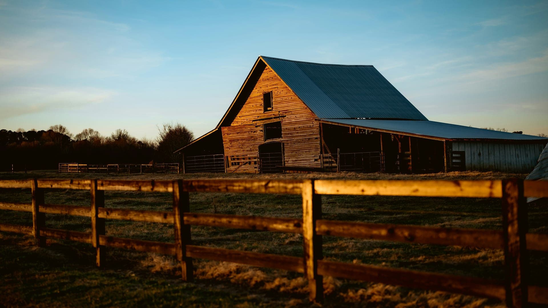 Weathered wooden barn behind a split-rail fence at golden hour